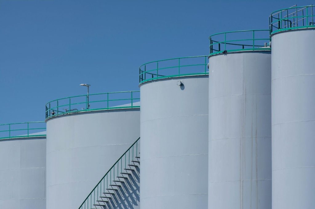 Exterior of an industrial facility with large vertical storage tanks under a clear blue sky, representing large-scale operations that rely on energy-efficient electric motors.