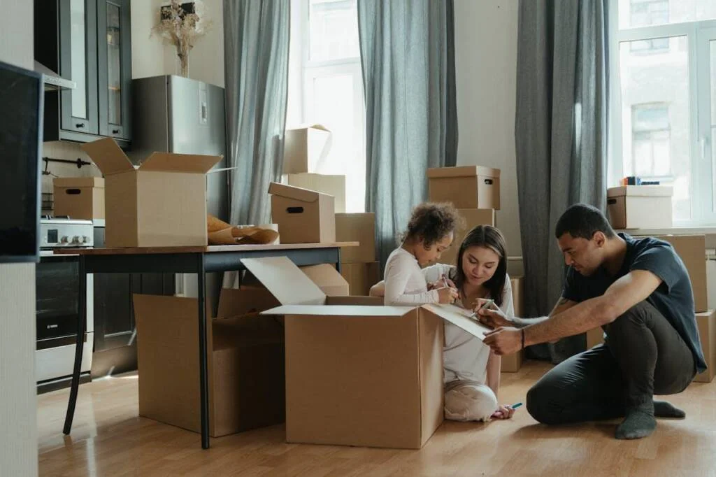 Creating Family Rituals That Make Any New Place Feel Like Home Family with cardboard boxes, unpacking, child coloring box, kitchen in new house