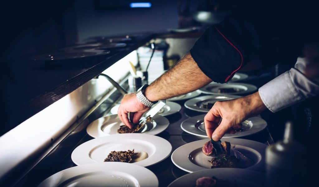 Restaurant Renovation Planning: How to Open on Time (and Stay Code‑Compliant) Chef plating food in a commercial kitchen designed by a restaurant contractor for efficient workflow and sanitation.