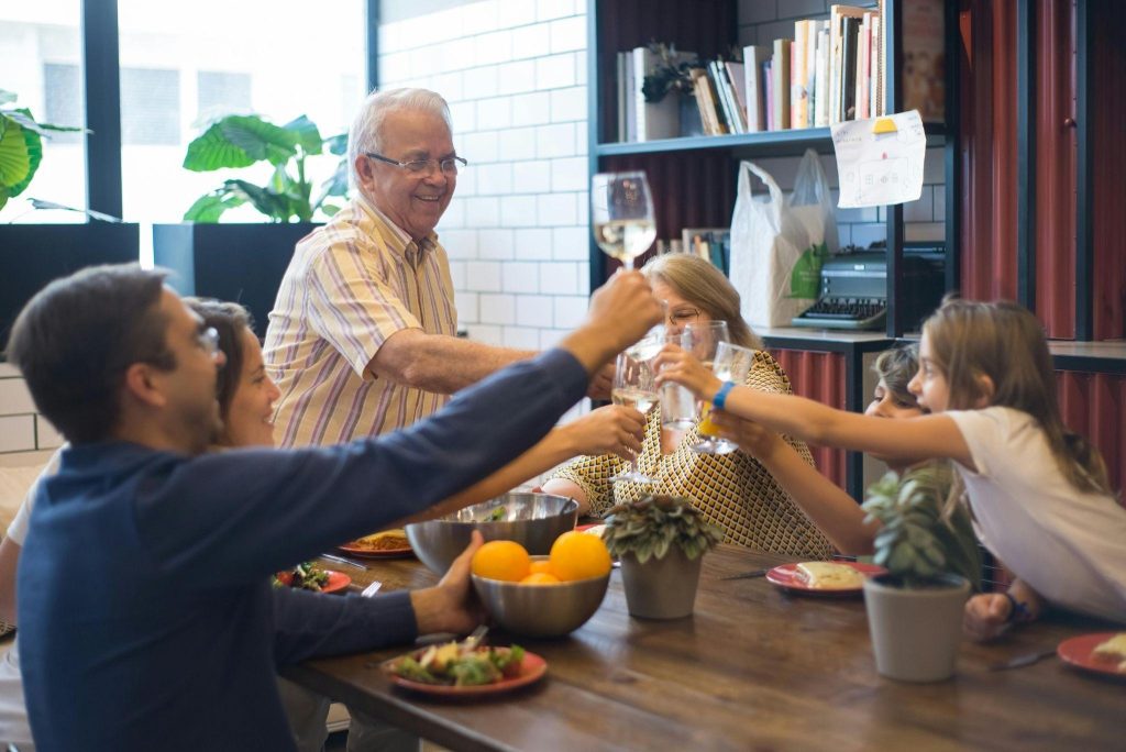  Senior man enjoying a family dinner at home with the assistance of a professional caregiver.
