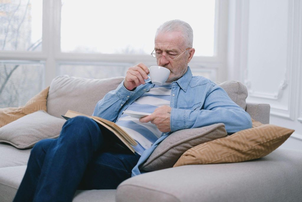 Older man relaxing at home in a comfortable chair, drinking coffee and reading a book.